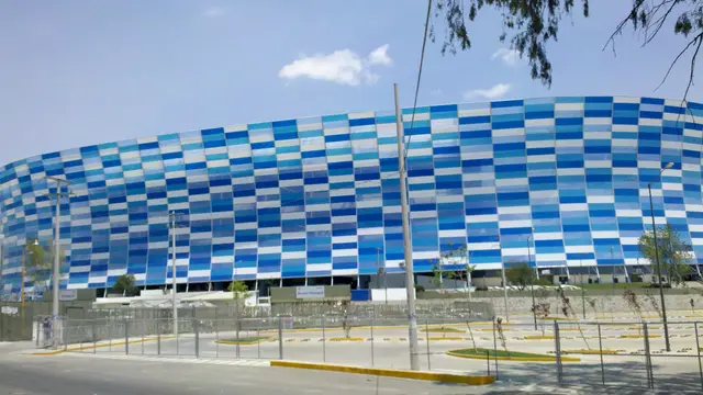 Fachada del Estadio Cuauhtémoc de Puebla, cubierta de paneles azules y blancos, vista desde el estacionamiento en un día soleado