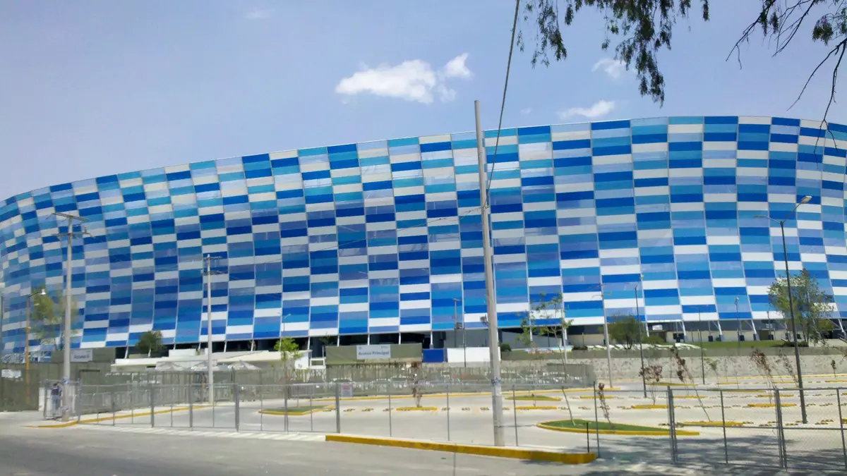 Fachada del Estadio Cuauhtémoc de Puebla, cubierta de paneles azules y blancos, vista desde el estacionamiento en un día soleado