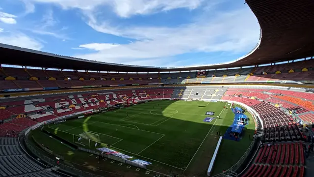 Interior del Estadio Jalisco en Guadalajara, casa actual del Atlas, con la cancha y las gradas rojas y blancas bajo un cielo azul