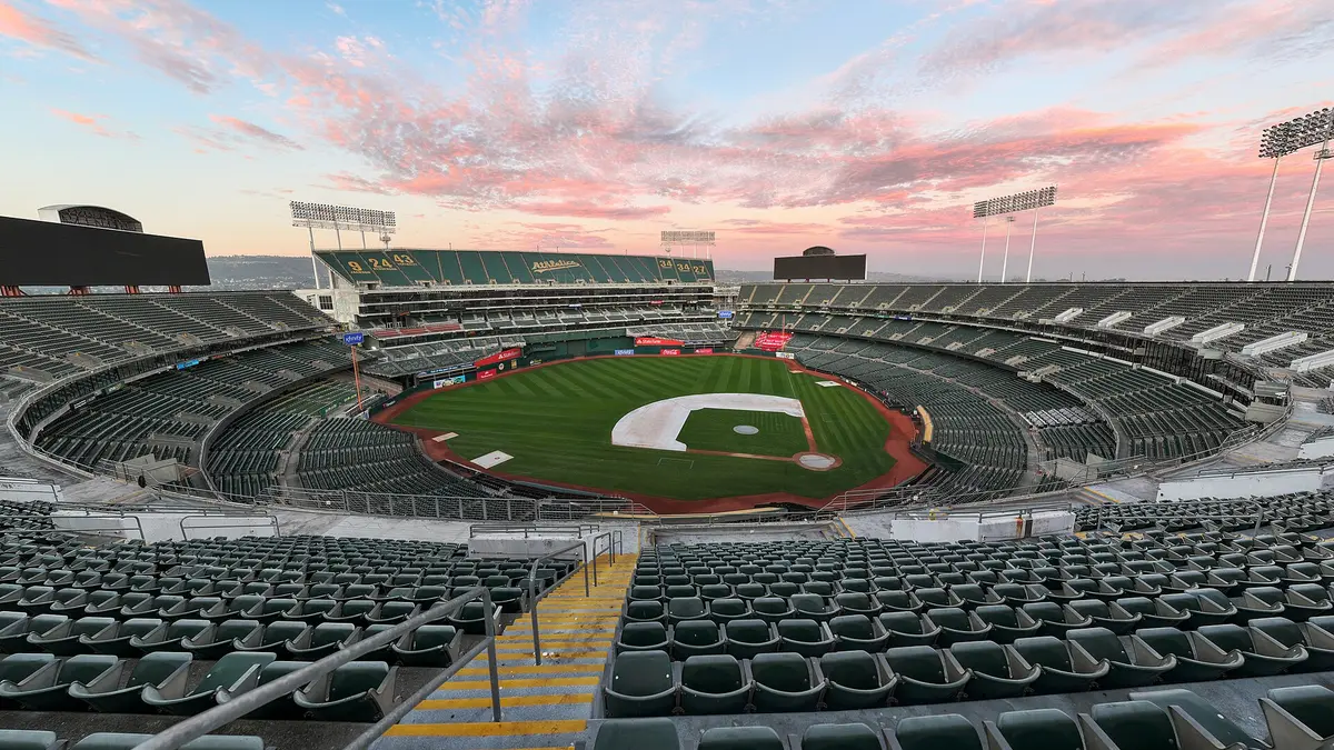 Vista desde la grada alta del Oakland Coliseum vacío al atardecer, con la cancha de pasto y el cielo rosado