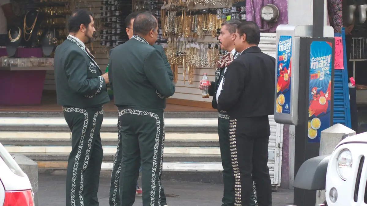 Mariachis con trajes de charro bordados y botonadura plateada platican en una calle