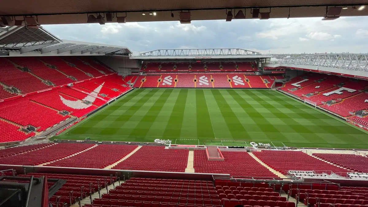 Interior del estadio Anfield vacío, con la cancha de césped rayado y las gradas rojas del Liverpool
