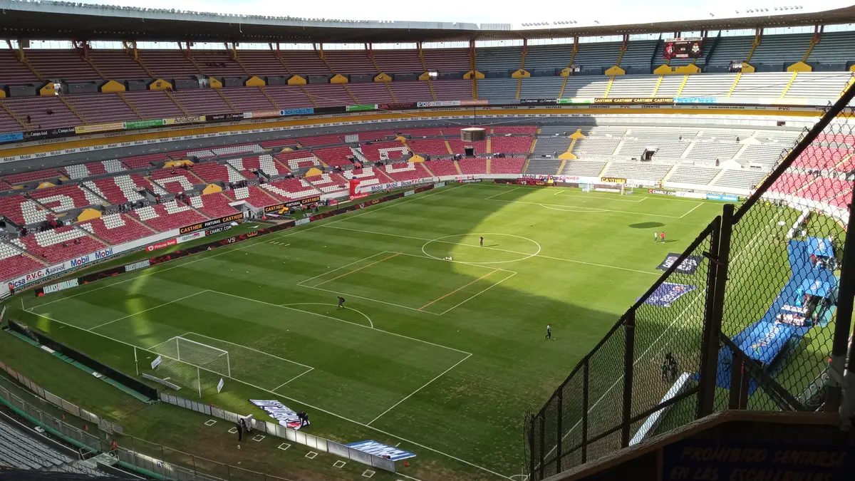 Vista desde la parte alta de la cabecera sur del Estadio Jalisco de Guadalajara, con la cancha y las tribunas rojas y blancas vacías