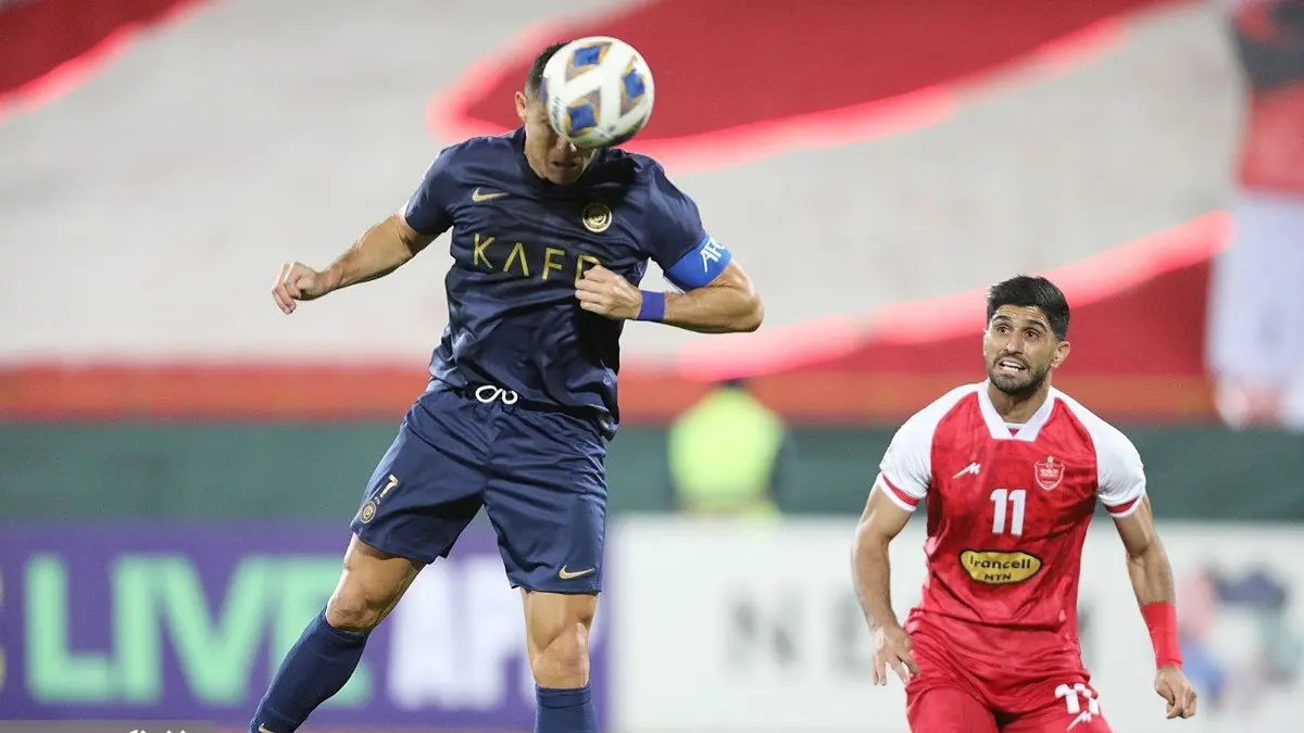 Cristiano Ronaldo, con la camiseta azul marino del Al Nassr y el gafete de capitán, cabecea el balón frente a un jugador del Persépolis vestido de rojo