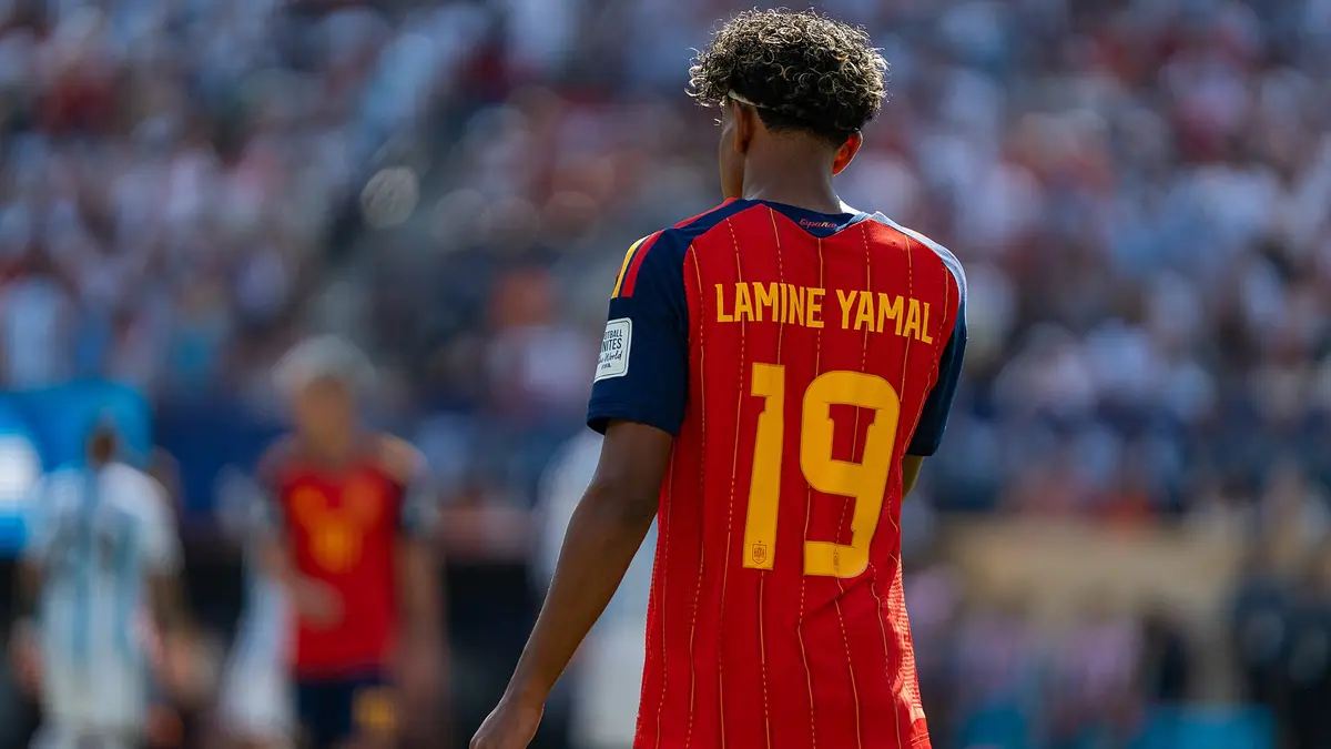 Lamine Yamal de espaldas con la camiseta roja número 19 de España durante un partido, con la tribuna llena al fondo