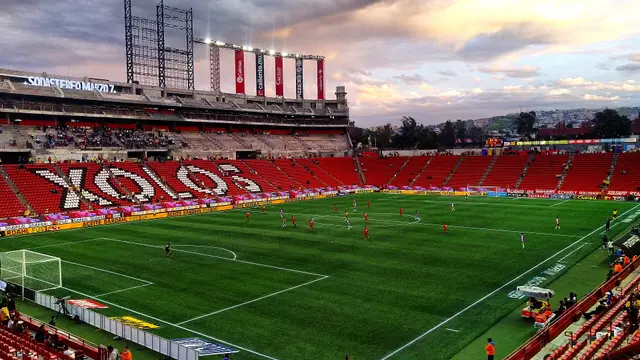 Estadio Caliente de Tijuana, casa de Xolos, con la palabra XOLOS en las gradas rojas durante un partido al atardecer