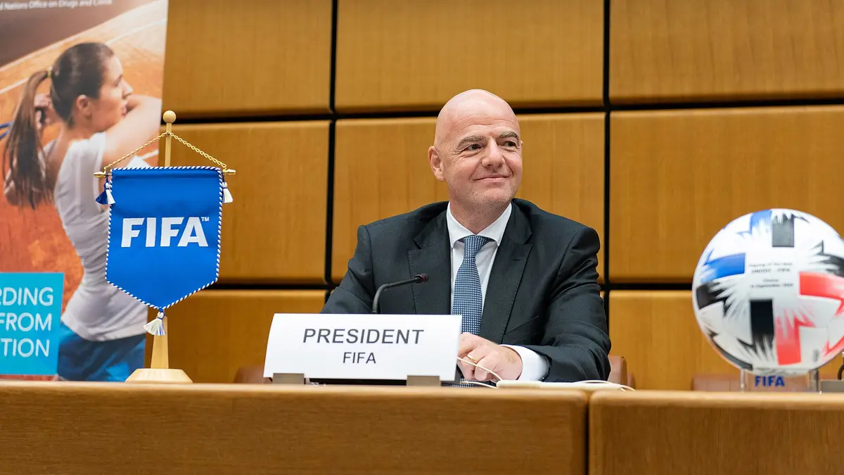 Gianni Infantino, presidente de la FIFA, sentado tras un letrero de President FIFA, con un banderín de la FIFA y un balón sobre la mesa