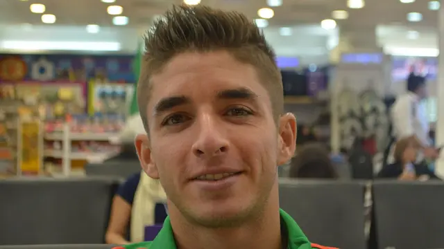 Isaac Brizuela sonríe con una chamarra verde de la Selección Mexicana en una sala de espera