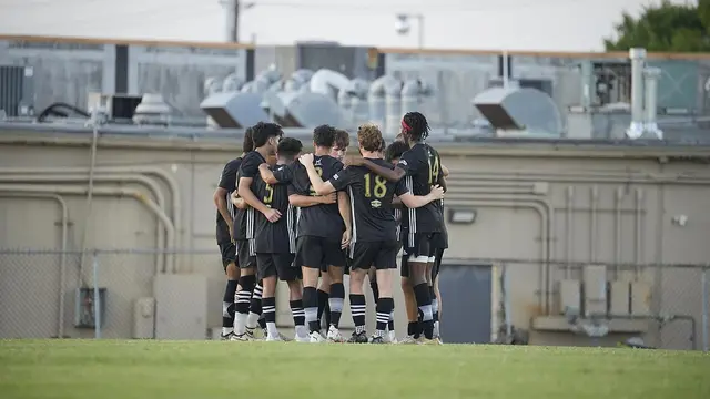 Jugadores de un equipo de futbol abrazados en círculo sobre el pasto durante el medio tiempo