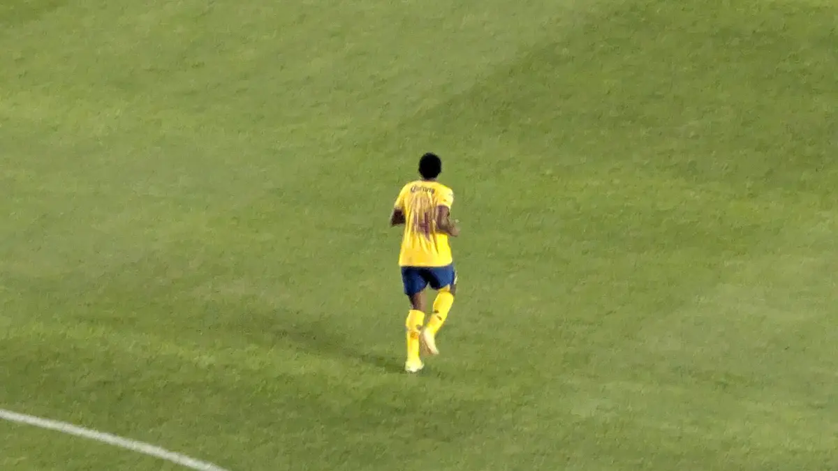 Una jugadora del América Femenil con uniforme amarillo y azul corre sola sobre el césped durante un partido ante Pachuca