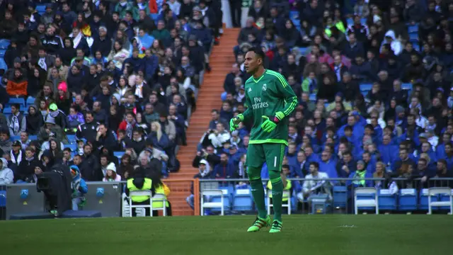 Keylor Navas, con uniforme verde de portero y guantes, de pie en la cancha durante un partido con el Real Madrid, con las gradas llenas al fondo