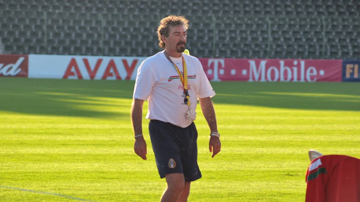 Ricardo La Volpe camina sobre el césped de un estadio con playera blanca y short azul durante un entrenamiento en junio de 2006