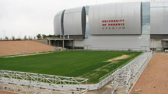 Cancha de pasto natural del estadio de Glendale, Arizona, sobre su bandeja retráctil afuera del inmueble, con la fachada plateada al fondo