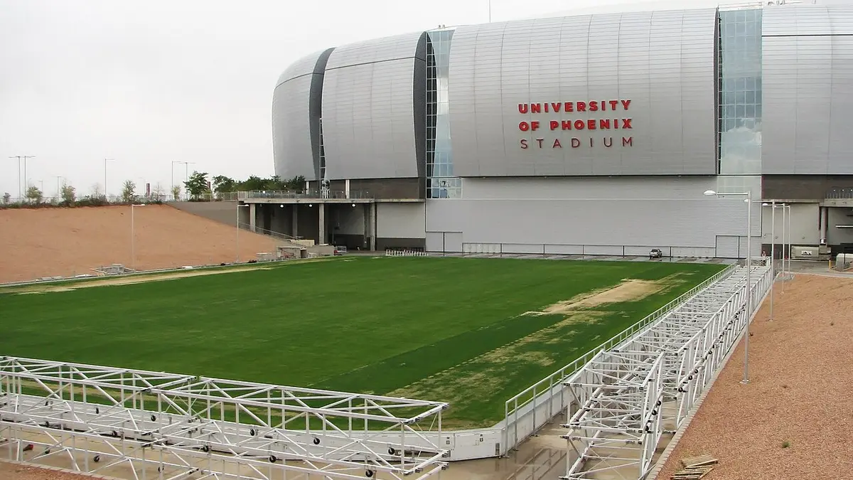 Cancha de pasto natural del estadio de Glendale, Arizona, sobre su bandeja retráctil afuera del inmueble, con la fachada plateada al fondo