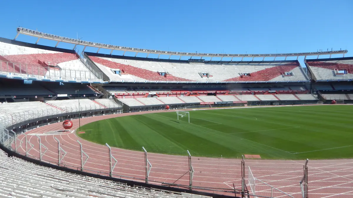 Interior del Estadio Monumental de River Plate en Buenos Aires en 2016, con la cancha verde, la pista de atletismo y las tribunas vacías bajo un cielo despejado