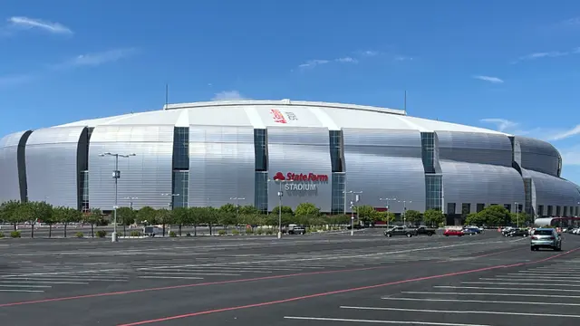 Exterior del State Farm Stadium en Glendale, Arizona, con su techo plateado y el estacionamiento vacío bajo cielo azul
