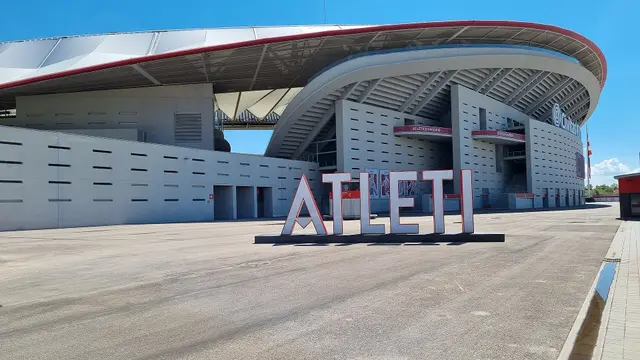 Exterior del Estadio Metropolitano del Atlético de Madrid en un día soleado, con letras gigantes que dicen ATLETI frente a la tribuna