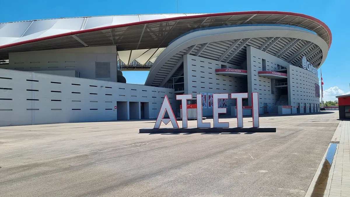 Exterior del Estadio Metropolitano del Atlético de Madrid en un día soleado, con letras gigantes que dicen ATLETI frente a la tribuna