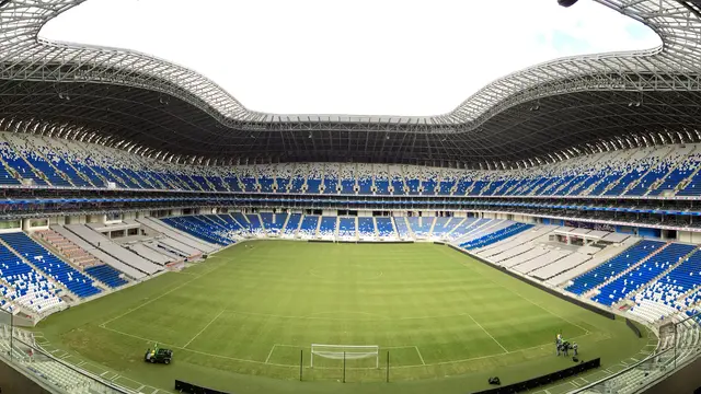 Vista panorámica del interior del Estadio BBVA en Guadalupe, Nuevo León, con la cancha verde y las gradas azules y blancas vacías