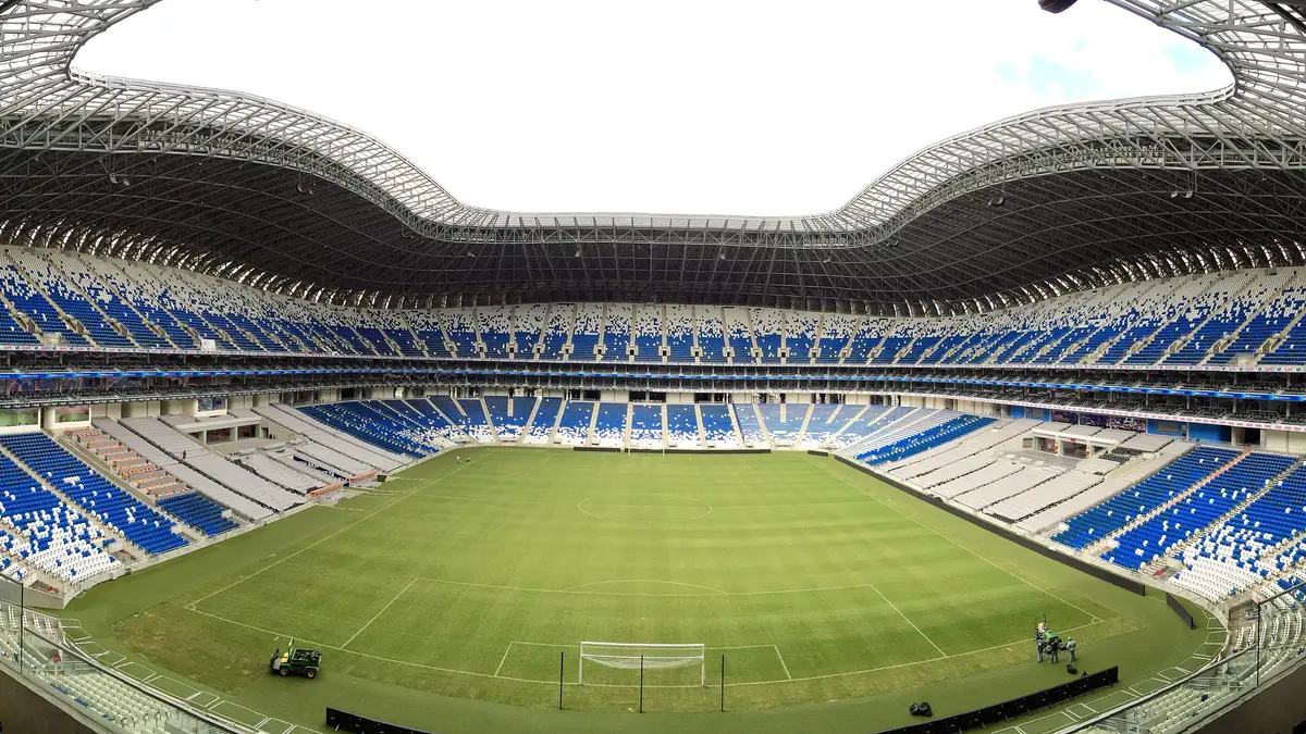 Vista panorámica del interior del Estadio BBVA en Guadalupe, Nuevo León, con la cancha verde y las gradas azules y blancas vacías