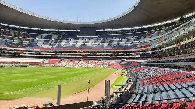 Interior del Estadio Azteca, hoy Estadio Banorte, con la cancha vacía y las gradas rojas y azules bajo el techo