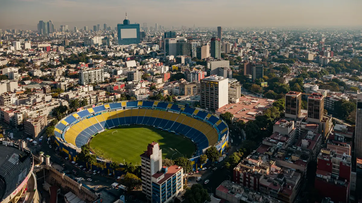 Vista aérea del Estadio Ciudad de los Deportes, con gradas azules y amarillas, rodeado de edificios de la Ciudad de México