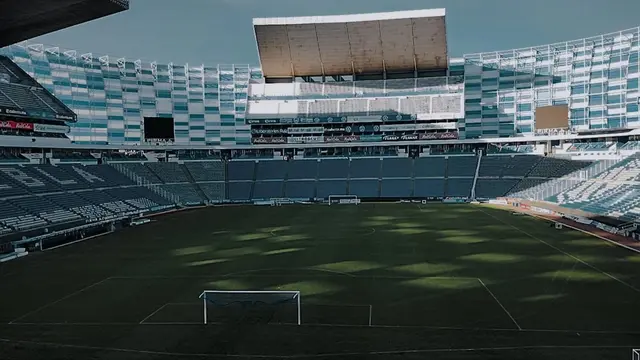 Interior del Estadio Cuauhtémoc de Puebla vacío, con la cancha, una portería y las gradas al fondo