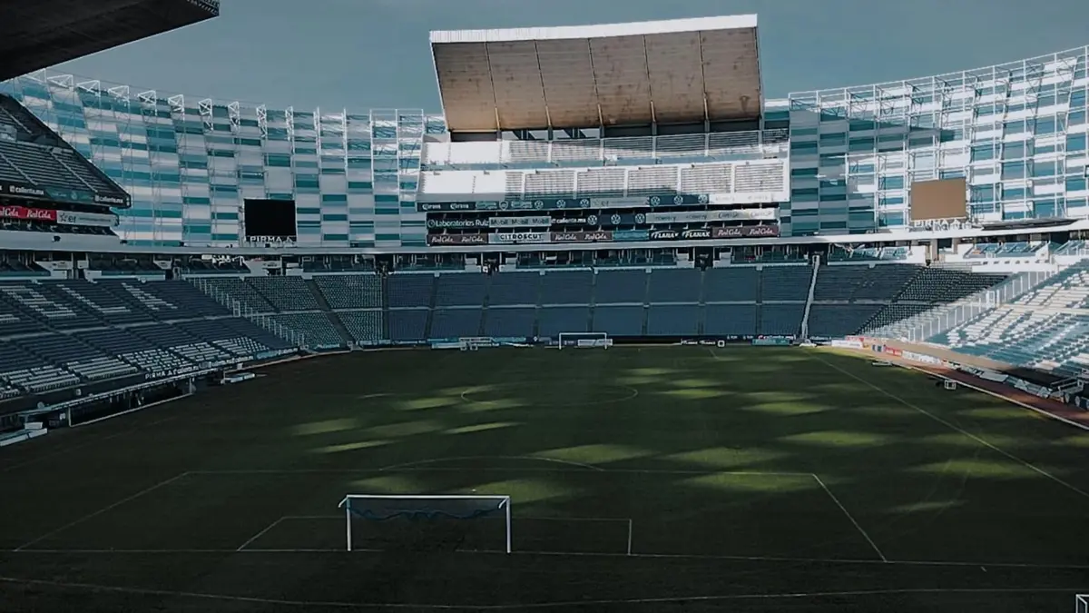 Interior del Estadio Cuauhtémoc de Puebla vacío, con la cancha, una portería y las gradas al fondo