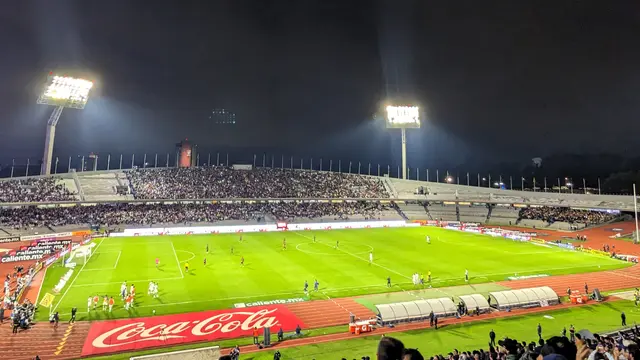 Vista nocturna del Estadio Olímpico Universitario durante un partido de Pumas, con las tribunas llenas, la cancha iluminada y las torres de luz encendidas