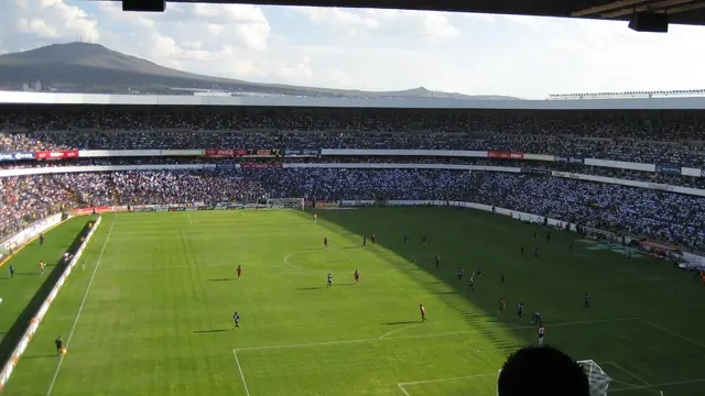 Vista desde la tribuna del Estadio Corregidora de Querétaro con la cancha, las gradas llenas y un cerro al fondo