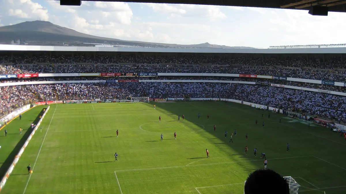 Vista desde la tribuna del Estadio Corregidora de Querétaro con la cancha, las gradas llenas y un cerro al fondo
