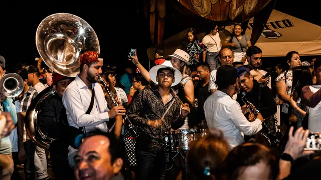 Músicos de una banda sinaloense con tuba, clarinetes y tarola tocando de noche entre el público del carnaval de Mazatlán