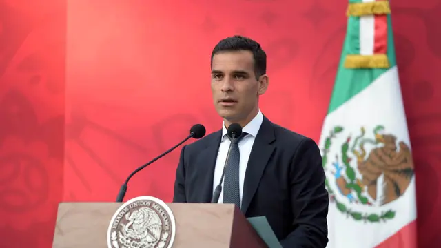 Rafael Márquez, de traje oscuro, habla detrás de un atril con micrófonos junto a una bandera de México