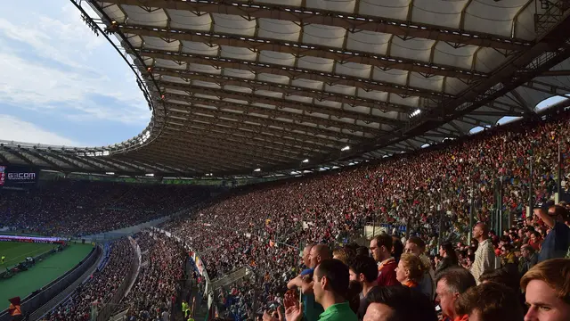 Tribunas llenas de aficionados en el Estadio Olímpico de Roma durante un partido de la AS Roma, con el techo del estadio iluminado por el sol