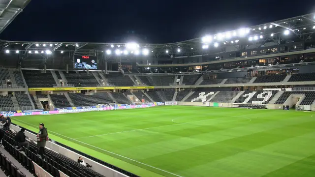 Interior de la Raiffeisen Arena de Linz, estadio del LASK, iluminada de noche con la cancha vacía y las gradas negras