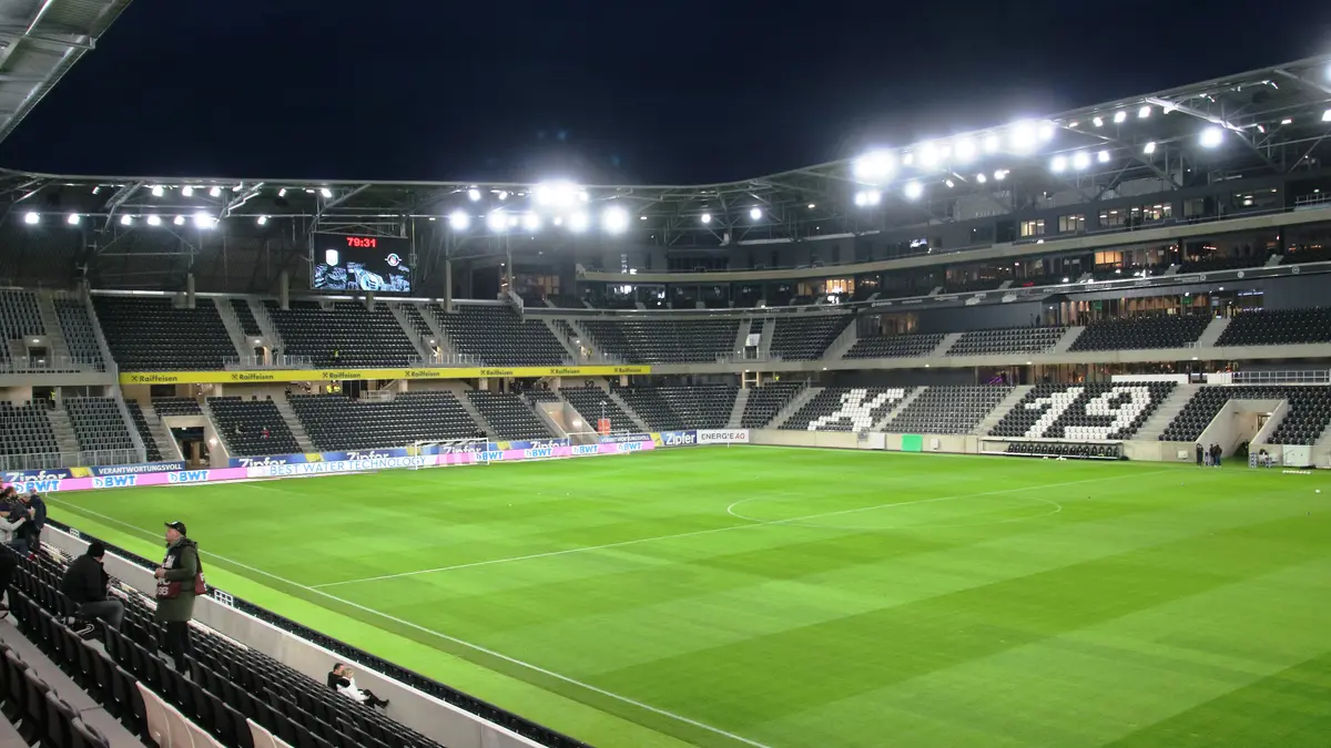 Interior de la Raiffeisen Arena de Linz, estadio del LASK, iluminada de noche con la cancha vacía y las gradas negras