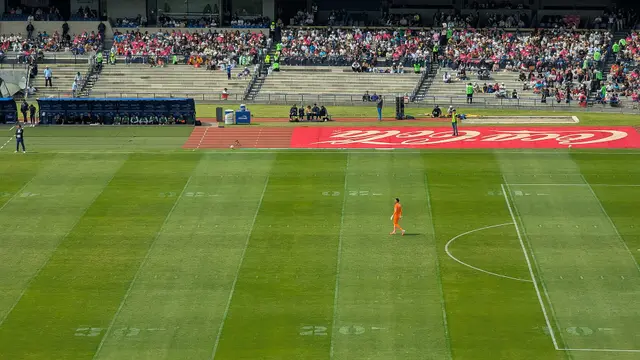 Cancha del Estadio Olímpico Universitario durante un partido de Liga MX, con un portero de naranja y las gradas al fondo