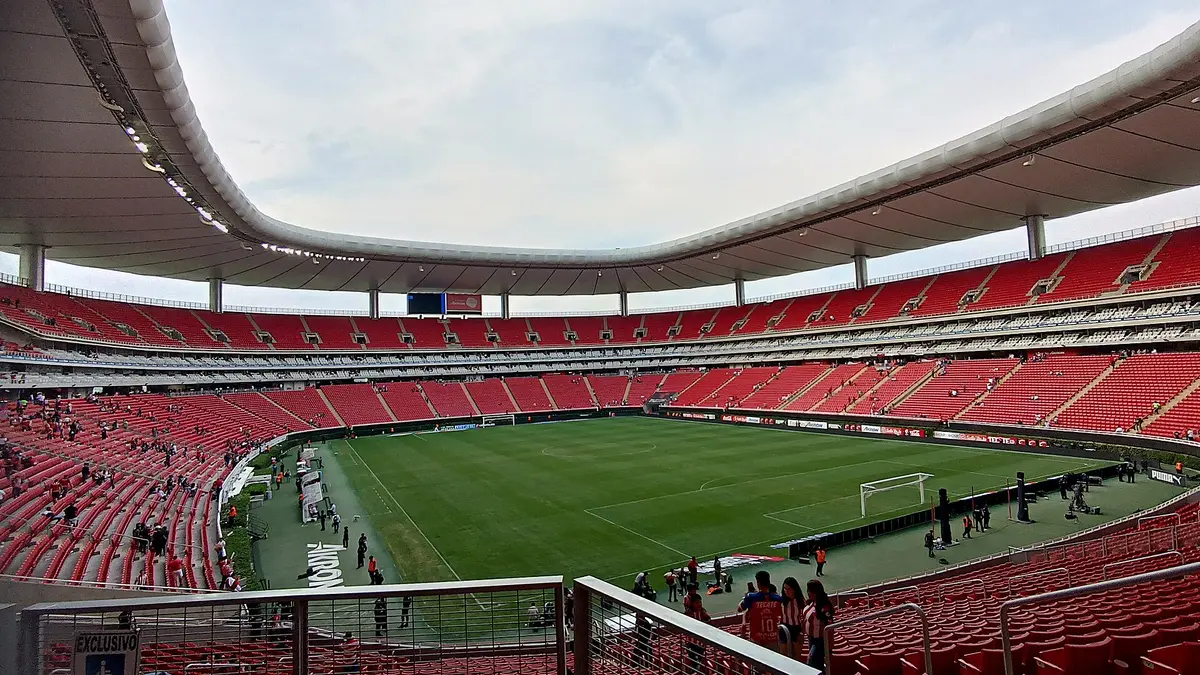Interior del Estadio Akron de Guadalajara con las tribunas rojas casi vacías y la cancha al fondo después de un partido