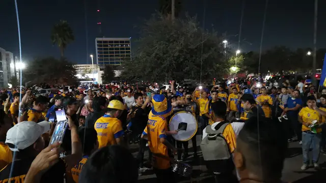 Aficionados de Tigres con playeras amarillas tocan tambores y celebran de noche en un estacionamiento antes de un partido de Tigres Femenil en 2022