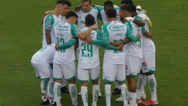 Jugadores del Club León con uniforme blanco y verde abrazados en círculo sobre el césped antes de un partido