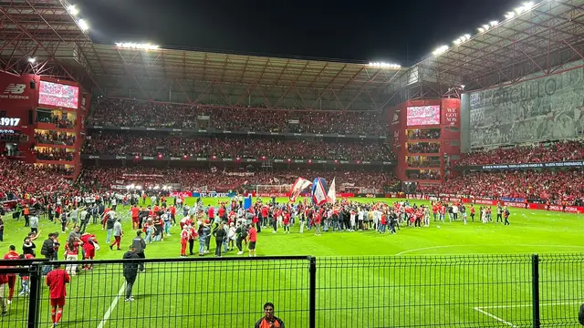 Estadio Nemesio Díez de Toluca de noche, con la tribuna llena y aficionados con playeras rojas sobre la cancha