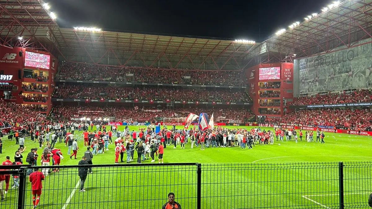 Estadio Nemesio Díez de Toluca de noche, con la tribuna llena y aficionados con playeras rojas sobre la cancha