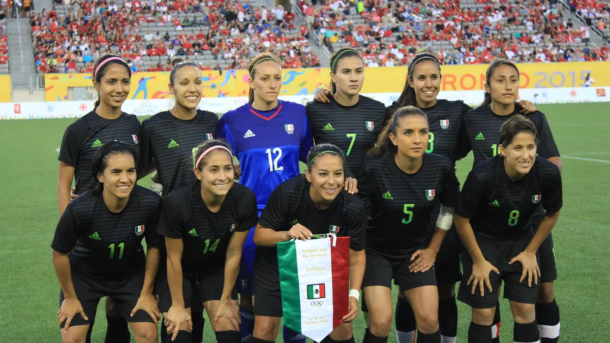 Las jugadoras titulares de la Selección Mexicana Femenil, con uniforme negro y un banderín de México, posan para la foto de equipo en los Juegos Panamericanos 2015
